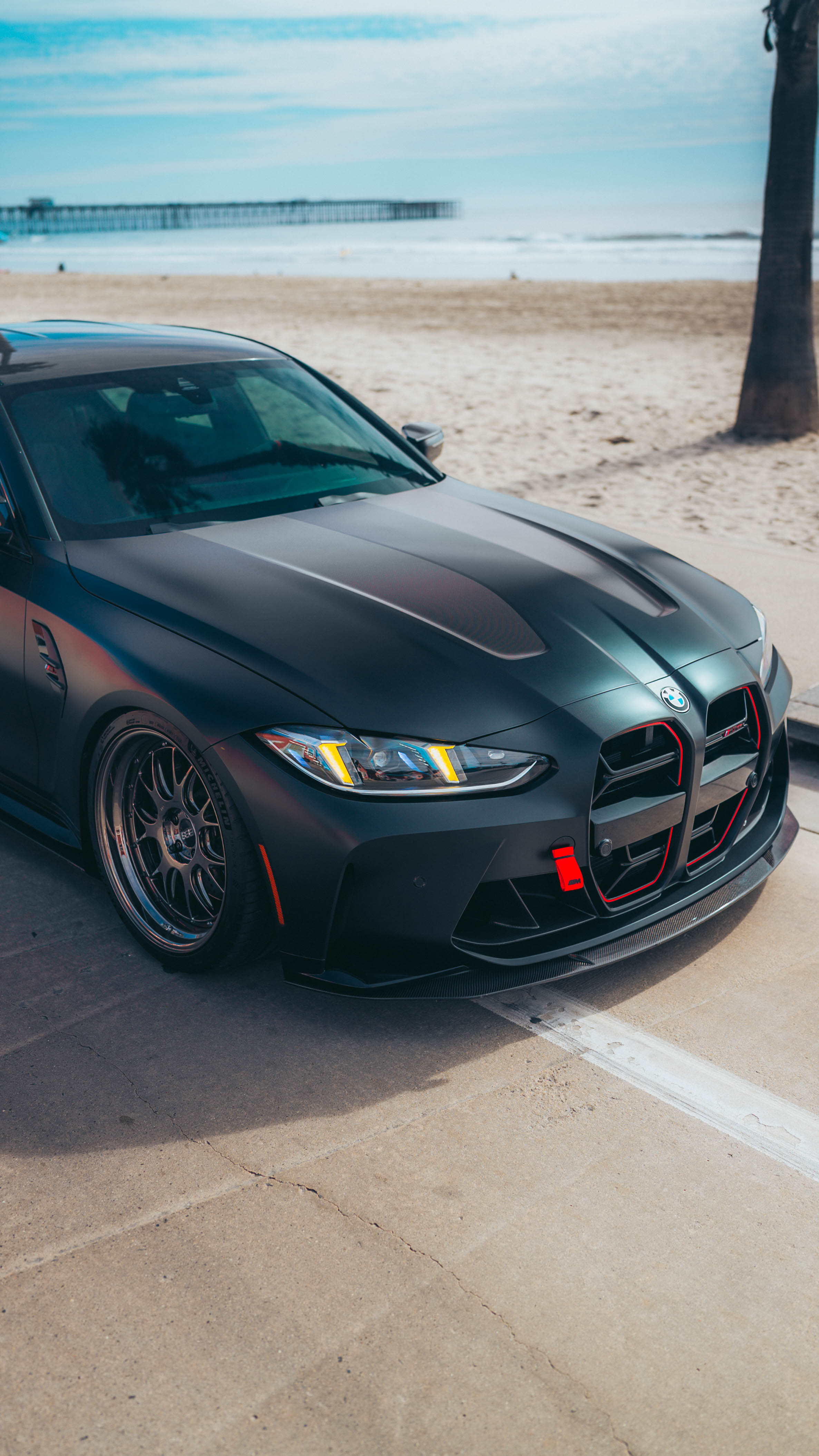 Black G80 M3 CS with snake eye headlights car parked on a beachside road with ocean and pier in the background